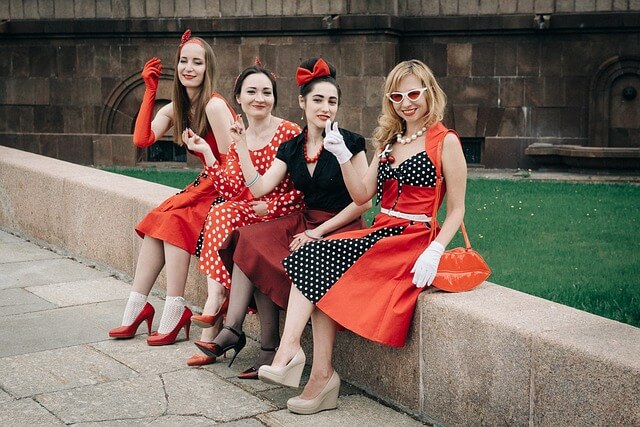 A group of women wearing vintage clothing sitting next to a garden